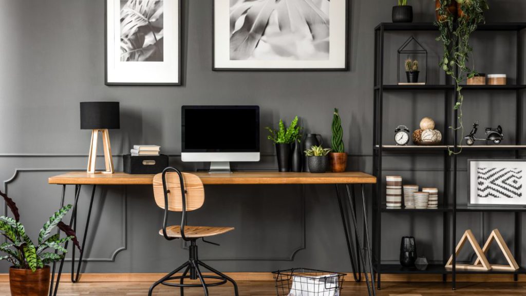 A home office with a wooden desk, adjustable chair, and computer sitting on the desk. Next to the desk is a shelving unit.