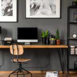 A home office with a wooden desk, adjustable chair, and computer sitting on the desk. Next to the desk is a shelving unit.