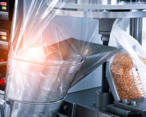 A close-up of a machine in a factory filling plastic bags with buckwheat and sealing them for distribution.