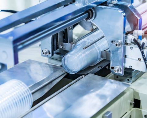 A stack of plastic food containers moving down a conveyor belt on a machine in a factory ready to be packaged.