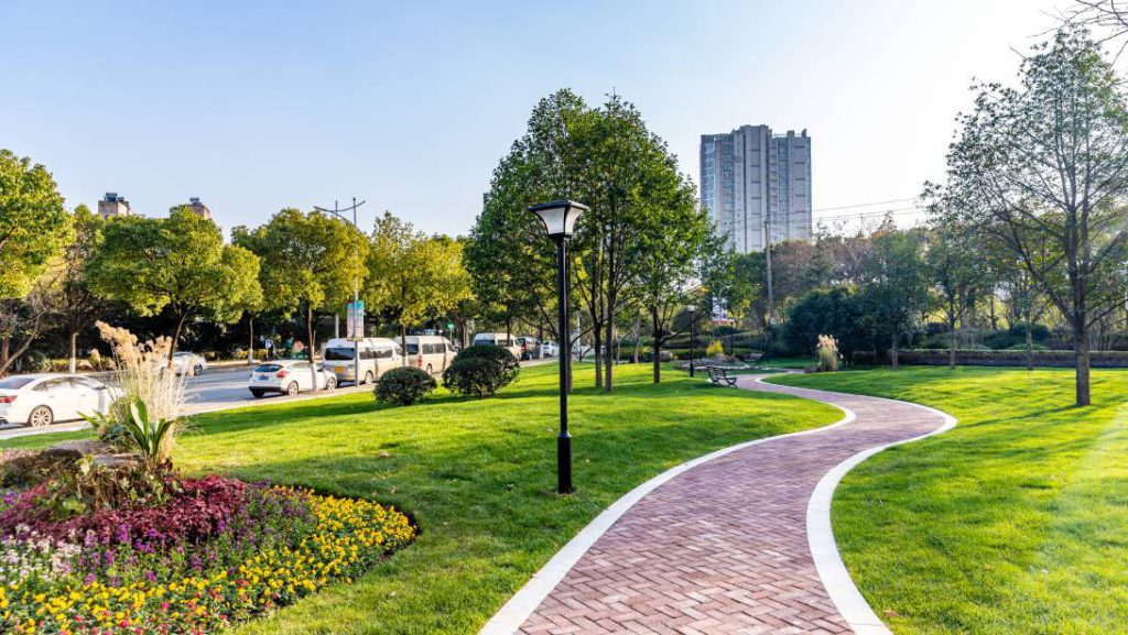 A beautiful landscaped outdoor area with a brick pathway in front of a modern commercial building and busy street.