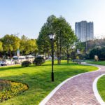 A beautiful landscaped outdoor area with a brick pathway in front of a modern commercial building and busy street.