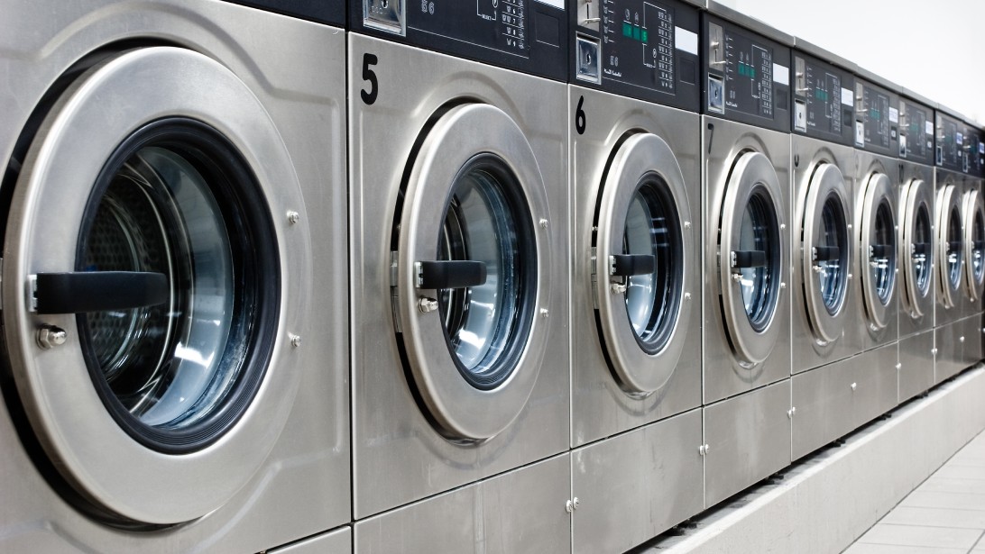 A brightly lit laundromat with a line of shiny, silver, numbered washing machines, open and ready for customers to use.