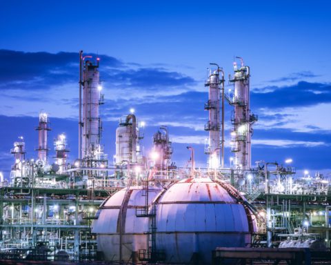A brightly lit chemical plant at night. The sky casts a purple glow on the two large storage spheres in the front.