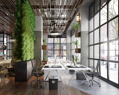 A contemporary office with ceiling to floor windows, multiple work stations, and greenery/plants everywhere.